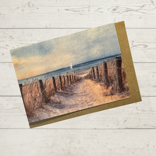 Image of actual card with natural kraft envelope. Image depicts a sandy path leading to a beach with sailboat in the distance.