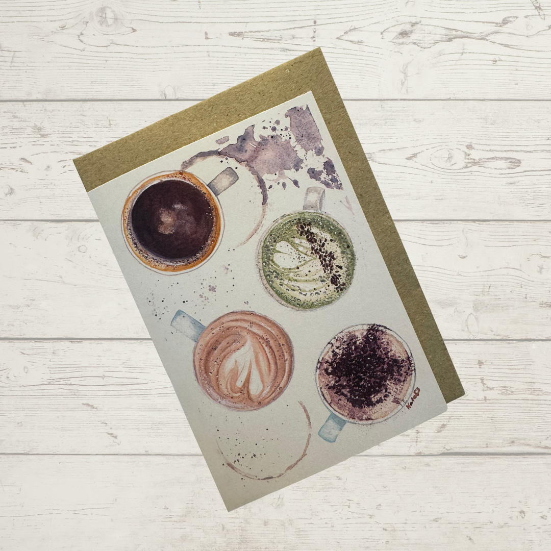 Image of actual card with natural coloured kraft paper envelope. Image depicts four coffee cups from a bird's eye perspective, with coffee spills from a long black, latte, matcha latte and cappuccino.