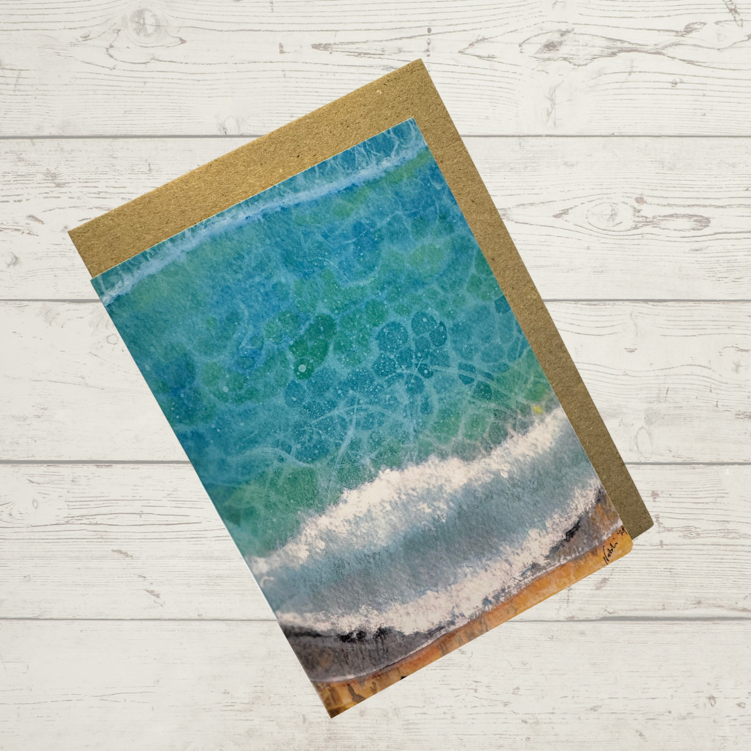 Image of actual card with natural coloured kraft paper envelope. Scene depicts dappled light in breaking waves on a beach from a bird's eye view.