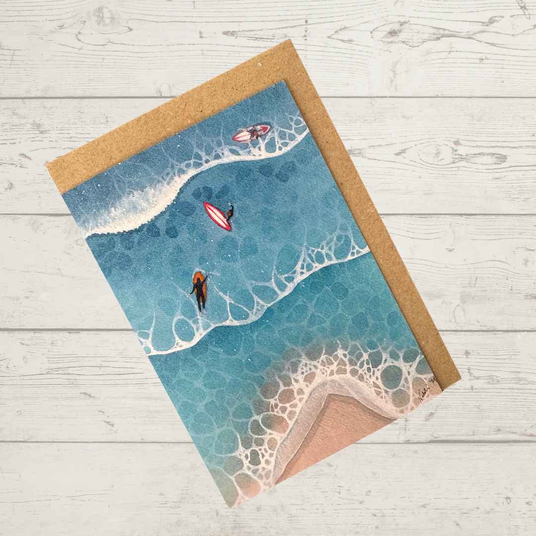 Image of actual card with natural coloured kraft paper envelope. Image depicts a whimsical interpretation of surfers paddling out to catch a wave as seen from a bird's eye view.